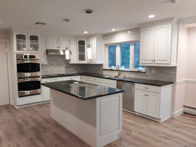 Modern kitchen with white cabinets, stainless steel appliances, black granite countertops, a center island, wood-look flooring, pendant lights, and a large window above the sink letting in natural light.
