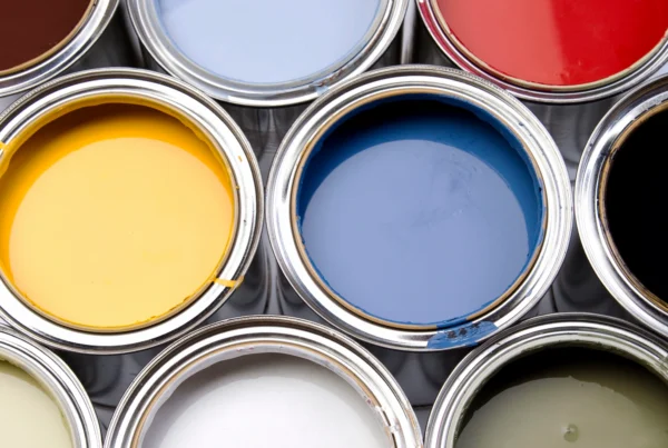 Open cans filled with vibrant Benjamin Moore paint colors by finish—yellow, blue, red, white, black, and other shades—are arranged closely together in a neat grid-like pattern.