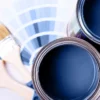 Open paint cans filled with blue paint, two paintbrushes, and a color swatch palette showcasing various shades of blue highlight the difference between flat matte, satin, and gloss paint finishes in this flat lay composition.