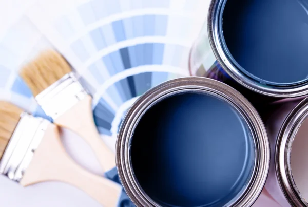 Open paint cans filled with blue paint, two paintbrushes, and a color swatch palette showcasing various shades of blue highlight the difference between flat matte, satin, and gloss paint finishes in this flat lay composition.