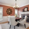 A dining room with four white upholstered chairs around a round table, set for a meal. The terracotta walls, carefully achieved by painting over dark colors, feature white trim, a decorative mirror, and a cozy fireplace with candles.